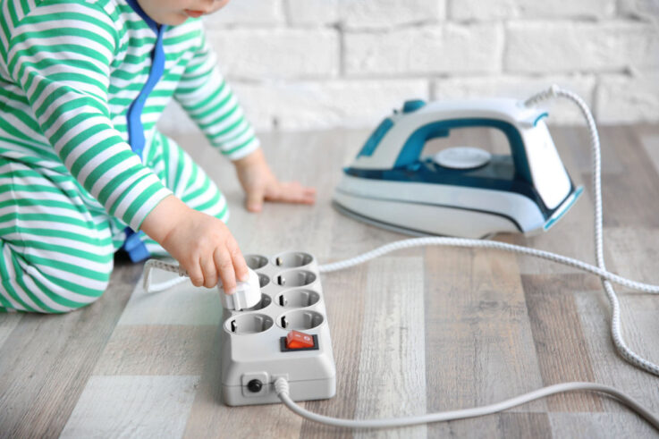 A baby playing with the plug of a clothes iron and trying to place it in an electrical strip